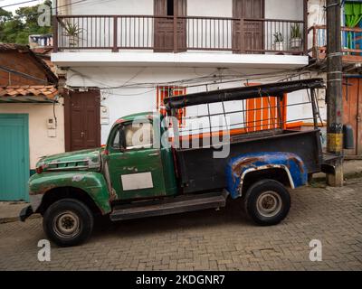 Jerico, Antioquia, Colombie - 5 avril 2022: Vieux camion vert ancien garé dans la rue coloniale étroite avec des maisons colorées Banque D'Images