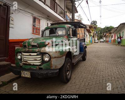 Jerico, Antioquia, Colombie - 5 avril 2022: Vieux camion vert ancien garé dans la rue coloniale étroite avec des maisons colorées Banque D'Images