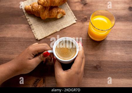 Mains de femme tenant une tasse de café chaud sur une table rustique en bois avec un jus d'orange et deux croissants Banque D'Images