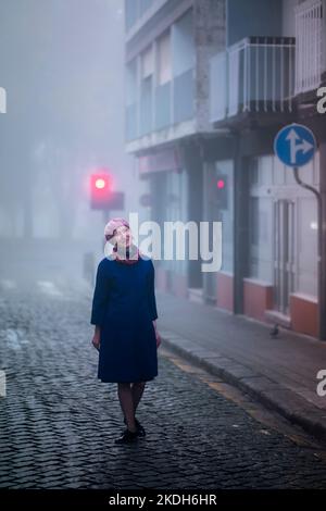 Une femme blonde sous un manteau se tient sur le trottoir dans le brouillard du matin. Banque D'Images