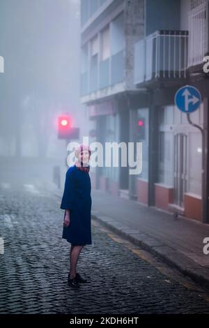 Une femme se tient sur le trottoir tôt le matin dans un épais brouillard. Banque D'Images