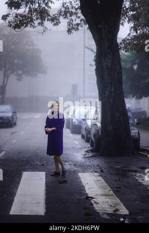 Une femme sous un manteau d'automne se tient à l'extérieur enveloppé dans le brouillard du matin. Banque D'Images