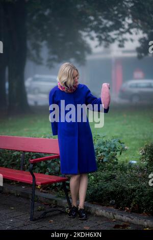 Une femme se tient à un banc de parc et tient un béret dans sa main. Banque D'Images