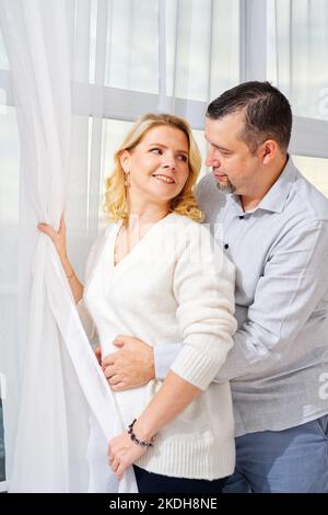Couple d'âge moyen embrassant devant la fenêtre. Portrait de femme et d'homme blond d'âge moyen Banque D'Images