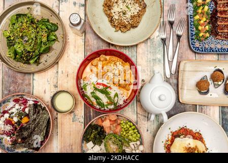 Ensemble de plats fusion avec un curry jaune de poulet avec du riz et des légumes, un bol de pêche au saumon, une salade, un risotto au fromage, des croquettes de moules et Banque D'Images