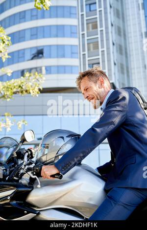 Homme d'affaires moderne en costume complet est assis sur la moto à l'extérieur Banque D'Images