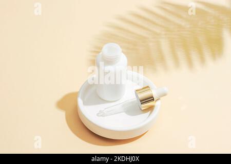 Flacon compte-gouttes blanc avec pipette et ombre à la fougères sur fond beige. Concept de cosmétiques anti-âge naturel. Gros plan. Banque D'Images