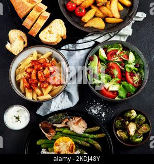 Ensemble de plats principaux variés. Différents plats sains, plats de viande et de poisson, pâtes, salades, sauces, pain et légumes sur fond sombre. À Banque D'Images