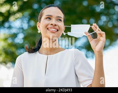 Covid, femme dans le parc qui prend son masque et célèbre la fin de la pandémie avec le sourire. Arbres, air frais et liberté du masque, femme d'affaires heureuse dans Banque D'Images