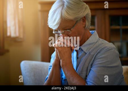 Vous n'êtes jamais vraiment seul si vous avez la foi. Une femme âgée regardant inquiet avec ses mains jointes ensemble à la maison. Banque D'Images