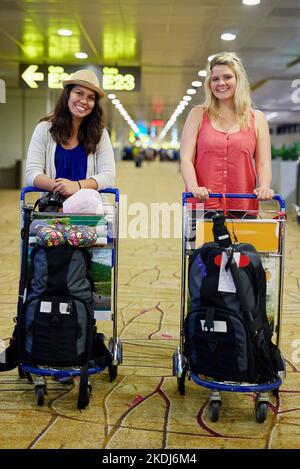 Emparés et prêts à partir. Deux jeunes amis qui poussent des valises dans des trolls tout en marchant ensemble à travers un aéroport. Banque D'Images