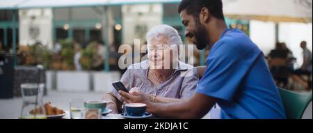 Aidant à prendre un café avec son client et à l'apprendre à l'aide d'un smartphone, à l'extérieur au café. Banque D'Images