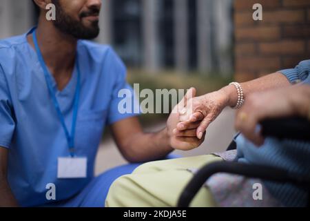 Gros plan du soignant tenant la main de son client sur un fauteuil roulant. Banque D'Images