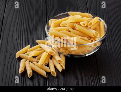 Pâtes de penne non cuites dans un bol en verre sur une table en bois noir Banque D'Images