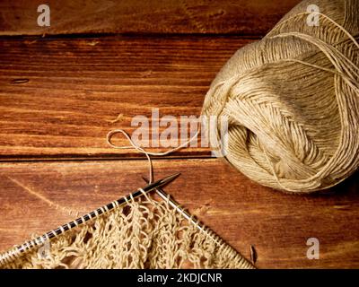 Processus de couture. Aiguilles à tricoter, boucles sur aiguilles à tricoter, tissu tricoté, pelote de fil, coton grossier et fil de lin, fond en bois Banque D'Images