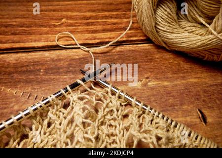 Nappe ajourée dans le processus de tricotage. Aiguilles à tricoter, boucles sur aiguilles à tricoter, tissu tricoté, pelote de fil, coton grossier et lin Banque D'Images