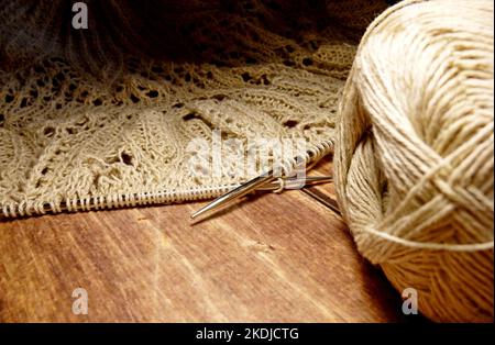 Nappe ajourée dans le processus de tricotage. Aiguilles à tricoter, boucles sur aiguilles à tricoter, tissu tricoté, pelote de fil, coton grossier et lin Banque D'Images