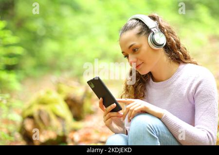 Femme détendue portant un casque d'écoute de musique et de contenu de téléphone dans une forêt Banque D'Images