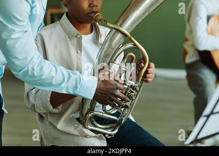 Gros plan de la main d'un jeune professeur de musique afro-américain qui aide un écolier pré-adolescent avec un instrument de vent pendant la leçon Banque D'Images