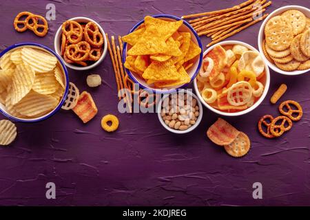 Chips de pommes de terre et de tortilla et autres en-cas salés, pris d'en haut avec espace de copie. Repas de fête sur fond violet. Un mélange de hors-d'œuvre dans des bols Banque D'Images