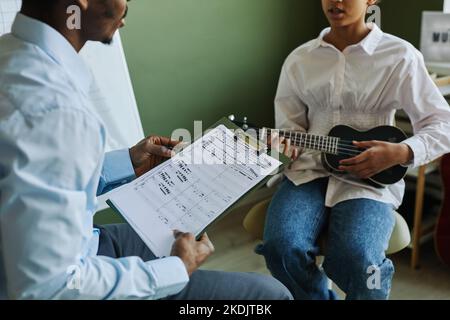 Gros plan du professeur de musique avec des notes musicales ayant une discussion avec une écolière jouant ukulele et consultant avec lui à la leçon Banque D'Images