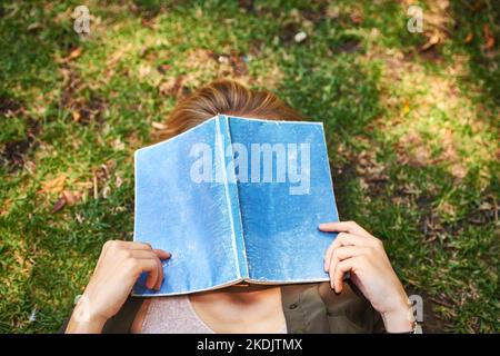 Ce livre est trop. Une femme méconnaissable lisant un livre tout en étant couché dehors sur l'herbe. Banque D'Images