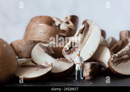 Champignons de châtaigne tranchés sur une planche à découper en ardoise, avec un chef miniature en uniforme Banque D'Images