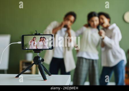 Écran de smartphone sur trépied avec trois écoliers qui exécutent des chansons ensemble tout en enregistrant des vidéos ou en faisant de la lecture en direct Banque D'Images