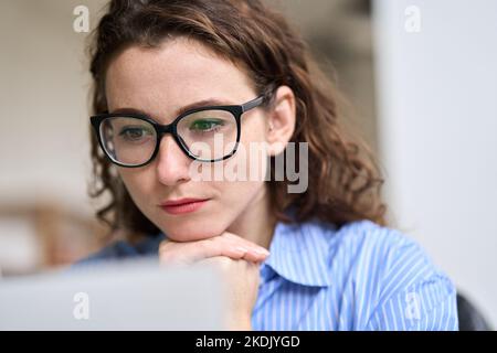 Jeune femme d'affaires portant des lunettes regardant un webinaire en ligne au travail. Banque D'Images