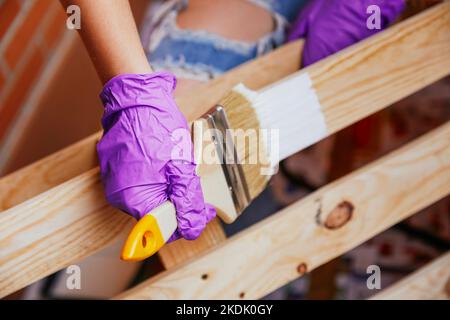 Gros plan des mains de femme méconnaissable avec des gants violets peignant une palette avec une brosse laissant une ligne blanche. Rénovations Banque D'Images