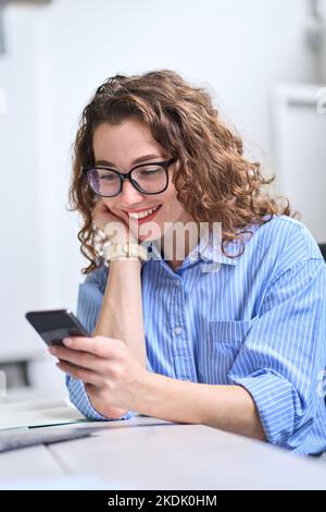 Une jeune femme d'affaires heureuse utilisant un téléphone cellulaire travaillant au bureau, à la verticale. Banque D'Images