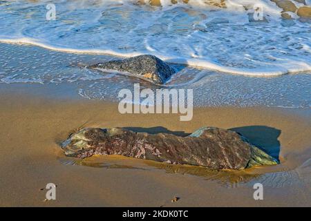 Surf en mer tourbillonnant autour de rochers isolés sur une plage de sable Banque D'Images