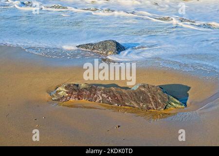 Surf en mer tourbillonnant autour de rochers isolés sur une plage de sable Banque D'Images