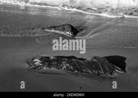 Surf en mer tourbillonnant autour de rochers isolés sur une plage de sable Banque D'Images