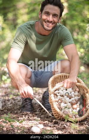 homme souriant d'âge moyen cueillant des champignons dans la forêt d'automne Banque D'Images