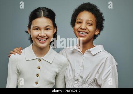 Deux filles chaleureuses et chaleureuses en chemises blanches rient et regardent la caméra tout en posant pendant la séance photo en studio Banque D'Images