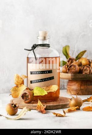 Délicieuse liqueur de medlar maison dans une bouteille de verre sur planche à découper en bois avec fruits frais. (Mespilus germanica). Espace pour le texte. Banque D'Images