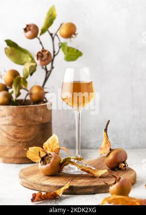 Vin maison ou liqueur de fruits medlar dans un petit verre avec fruits frais mûrs sur planche à découper en bois. (Mespilus germanica) espace de copie. Banque D'Images