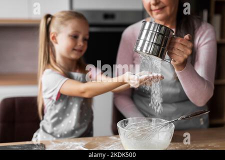 Bonne petite-fille caucasienne et grand-mère âgée préparent la pâte à cuire, verser la farine Banque D'Images