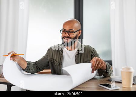 Ingénieur industriel latin mûr et heureux regardant les dessins de projet travailler à table, travailler à l'intérieur du bureau, copier l'espace Banque D'Images