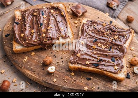 Planche de pain avec pâte de chocolat et bonbons de fête saupoudrer et noisettes sur fond de bois. Nourriture populaire de dessicer. Vue de dessus. Banque D'Images