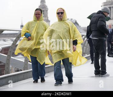 Les personnes portant des ponchos pendant une douche à effet pluie, sur le Millennium Bridge à Londres. Date de la photo: Lundi 7 novembre 2022. Banque D'Images