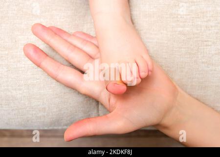 La mère colle un pansement médical adhésif sur la jambe du bébé. Main de maman avec ruban adhésif de protection collant et pied d'enfant. Enfant âgé de un vous Banque D'Images