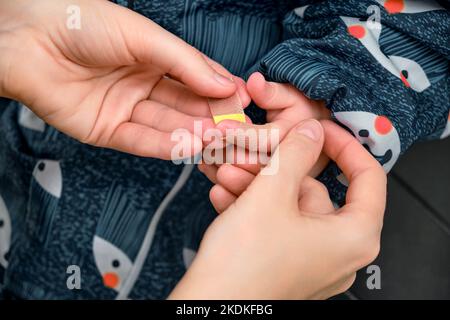 Une mère-femme colle un plâtre sur le doigt d'un bébé dans des vêtements chauds Banque D'Images