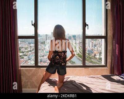 Vue arrière d'une femme caucasienne regardant par la fenêtre à l'horizon de Ho Chi Minh ville, Vietnam - concept d'isolement à la maison Banque D'Images