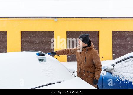 Un jeune homme nettoie la neige de sa voiture. Entretien de la voiture en hiver Banque D'Images