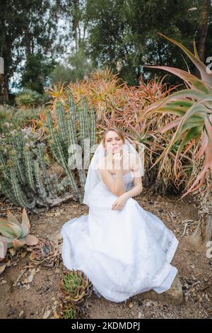 Mariée dans le mariage blanc Gown assis entouré par le jardin de Cactus Banque D'Images