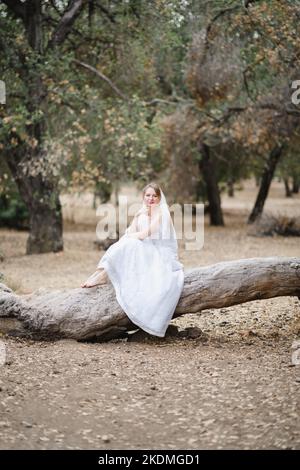 Mariée assise sur un grand arbre tombé dans le bosquet des chênes de Californie Banque D'Images