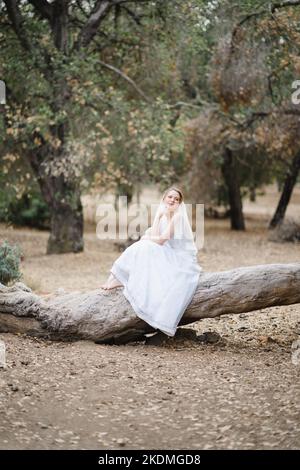 Mariée assise sur un grand arbre tombé dans le bosquet des chênes de Californie Banque D'Images