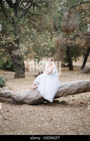 Mariée assise sur un grand arbre tombé dans le bosquet des chênes de Californie Banque D'Images